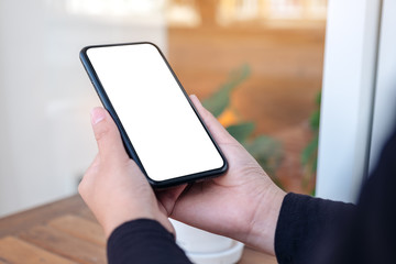 Mockup image of hands holding black mobile phone with blank white desktop screen in the outdoors