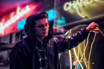 A pensive young man leaning on an illuminated signboard in the street at night.