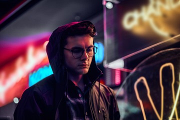 A handsome young man standing at night in the street. Illuminated signboards, neon, lights.