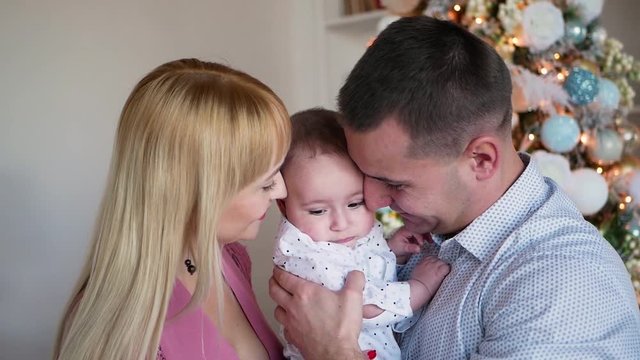 parents hold their son in the hands of standing in the room at the christmas tree