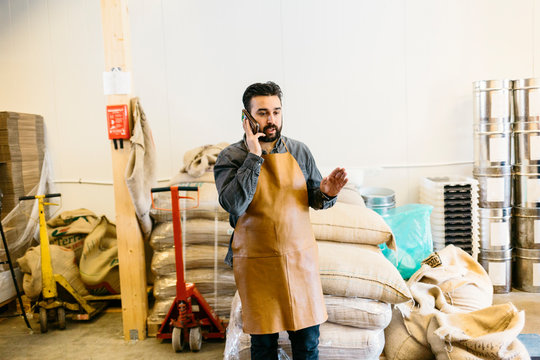 Small business owner in his coffee roaster shop talking on his cell phone