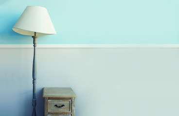 Floor torch lamp, wooden nightstand, curtains on pastel blue wall background. Banner with copy...