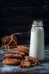 Oatmeal cookies with raisins, chocolate and milk in bottles, wood background
