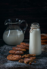 Oatmeal cookies with raisins, chocolate and milk in bottles, wood background