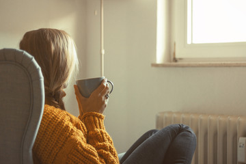 Junge Frau schaut aus dem Fenster und trinkt eine Tasse Tee