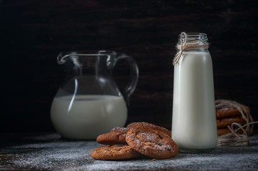 Oatmeal cookies with raisins, chocolate and milk in bottles, wood background