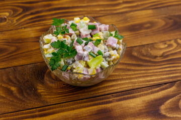Tasty salad with sausage, green pea, canned corn, bell pepper, cucumber and mayonnaise on wooden table