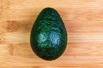 a single whole Hass Avocado on a bamboo  cutting board ready to be sliced, peeled and used in a dish, a salad or eaten alone.