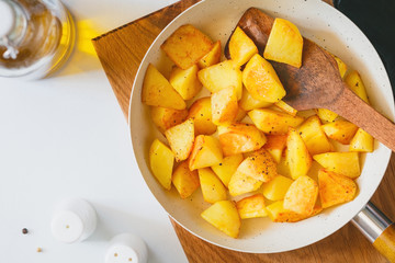 Top view on roasted potato in a white pan on a kitchen table. Modern style, vegetarian food.
