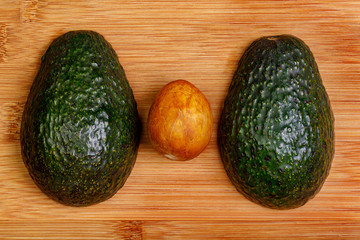 Two halves of an avocado face down on a bamboo cutting board with the pit on the surface between them.