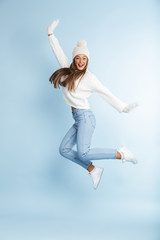 Cute young woman wearing winter hat jumping isolated over blue wall background.