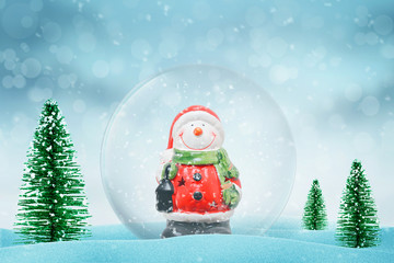 Christmas magic snow ball with Snowman. Snow falls in background. Christmas trees beside.
