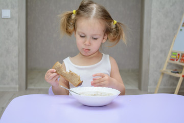 Child eating soup at home. Little girl have a dinner. Funny kid with piece of bread and plate of...