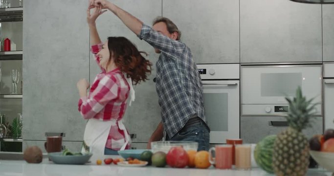 Modern gray kitchen charismatic couple dacing in front of the camere while preparing the food.