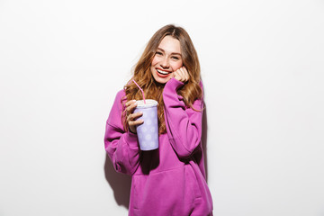 Fototapeta premium Portrait of adorable woman 20s wearing sweatshirt drinking soda from paper cup using straw, isolated over white background