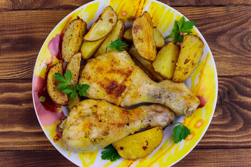 Baked chicken drumsticks with potatoes in a plate on wooden table