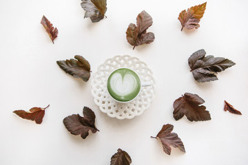 Fresh useful green matcha latte coffee in a beautiful mug. Nearby lie autumn leaves. Simple minimalistic autumn design.