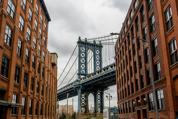 Manhattan Bridge Viewed From Dumbo, Brooklyn, New York between two red brick buildings and cloudy background