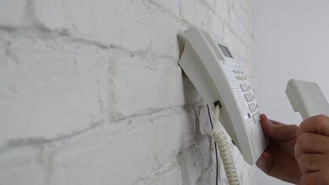 Man Inside Office Room Use a Telephone Fixed on the Wall to Make a Phone Call