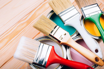 Four open cans of paint with brushes on them on wooden natural background. Yellow, white, pink, turquoise colors. Macro