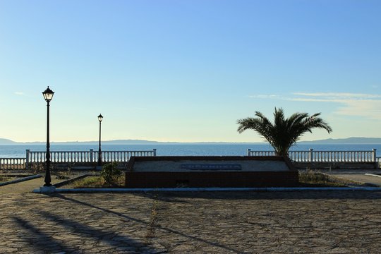 &Alpha;mbracian gulf behind the concrete retro fence made of cement from the square of Koronisia village lamps in the foreground square paved with stones on the sign "Koronisia" in Greek language in Greece