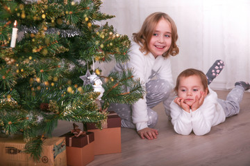 Two adorable little sisters looking for gifts under a Christmas tree on Christmas eve at home