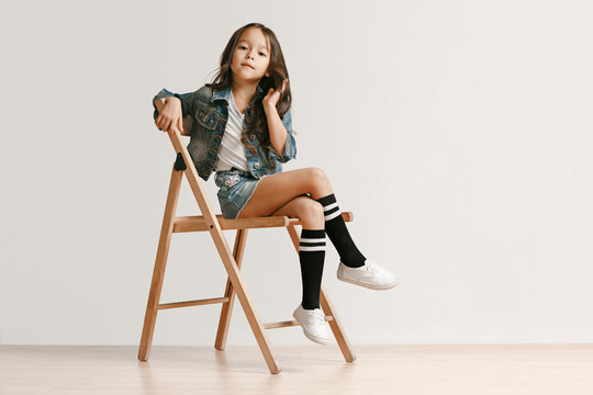 Full length portrait of cute little kid girl in stylish jeans clothes looking at camera and smiling against white studio wall. Kids fashion concept