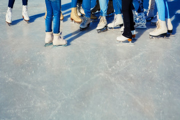 Close-up of the skates from the skaters on the ice surface. Skate on the ice in the company of friends. Skate rental. Place for text.