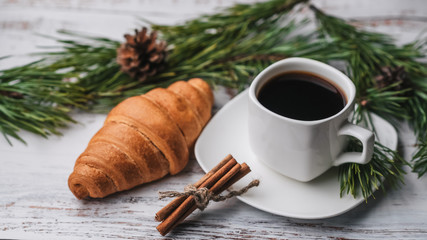 Obraz na płótnie Canvas Cup of coffee and a croissant in new year decor. Christmas winter holiday Breakfast decorated with pine branches and cones