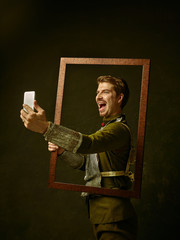 Medieval knight with mobile phone on dark studio background. Portrait in low key of brutal man in...
