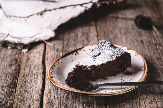 Kladdkaka. Traditional Swedish moist chocolate cake on old rustic wooden table decorated dry twigs, pine cones and birch bark. Fika. Hygge. Toned image