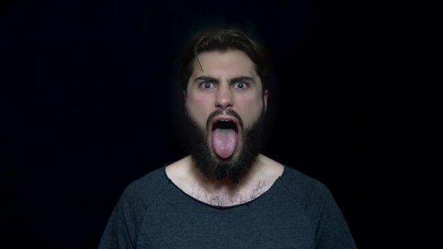 Young man with beard and tongue sticking out in rage. Angry young man to madness with open mouth. Human facial expressions and emotions