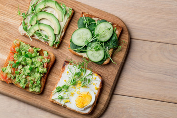 Fresh avocado toasts with different toppings. Healthy vegetarian breakfast with rye whole grain sandwiches