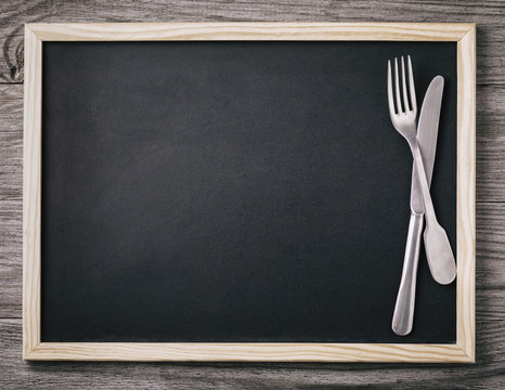 Empty menu blackboard with knife and fork on wooden background. Food background
