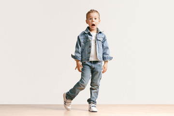 The portrait of cute little kid boy in stylish jeans clothes looking at camera against white studio wall. Kids fashion concept © master1305