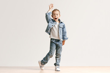 Fototapeta premium The portrait of cute little kid boy in stylish jeans clothes looking at camera against white studio wall. Kids fashion concept