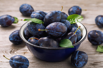Full bowl of freshly harvested ripe prune fruits on wooden table closeup