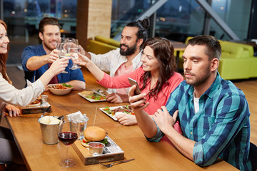 technology, lifestyle and people concept - man dining with friends and messaging on smartphone at restaurant