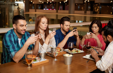 leisure, technology, lifestyle and people concept - friends with smartphones dining at restaurant