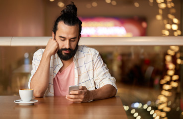 people, technology and leisure concept - man drinking coffee and messaging on smartphone at restaurant or cafe