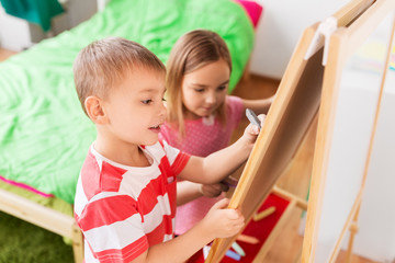 childhood, leisure and people concept - happy kids drawing on easel or flip board at home
