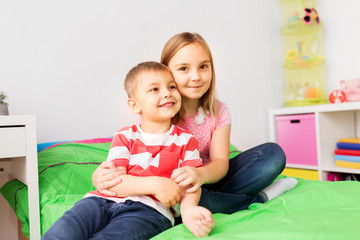 childhood, leisure and family concept - happy little kids hugging at home