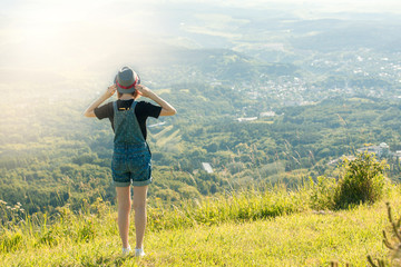 Fototapeta na wymiar Girl with a backpack and a hat standing with her back against a background of green mountains.