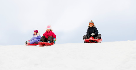 Fototapeta na wymiar childhood, sledging and season concept - group of happy little kids sliding on sleds down snow hill in winter