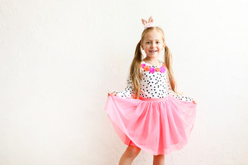 Portrait of cute little five year old girl with long blond hair wearing easter bunny ears on head, colorful polka dot shirt and pink tutu skirt. White wall backgroung, copy space, close up.