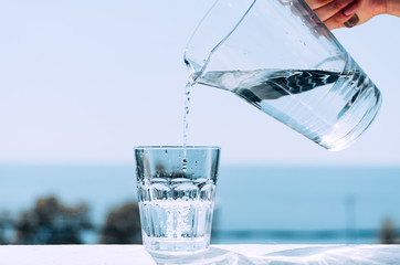 Pure water from a jug is poured into a glass beaker. Glass with water on the background of the sea.
