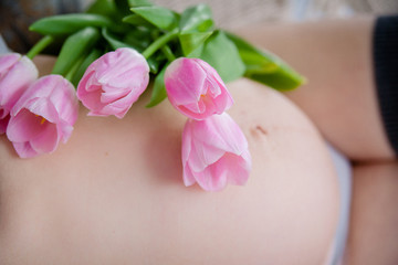 a bouquet of tulips lies on the belly of a pregnant woman