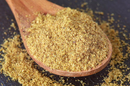 Ground cumin powder in wooden spoon on dark background