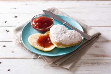 Romantic breakfast with heart-shaped bun, berry jam and roses on white wooden table