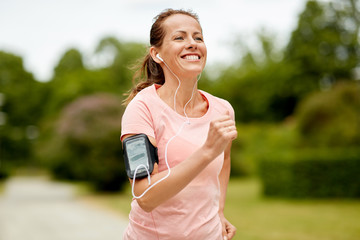 fitness, sport and healthy lifestyle concept - smiling woman with earphones wearing armband for...